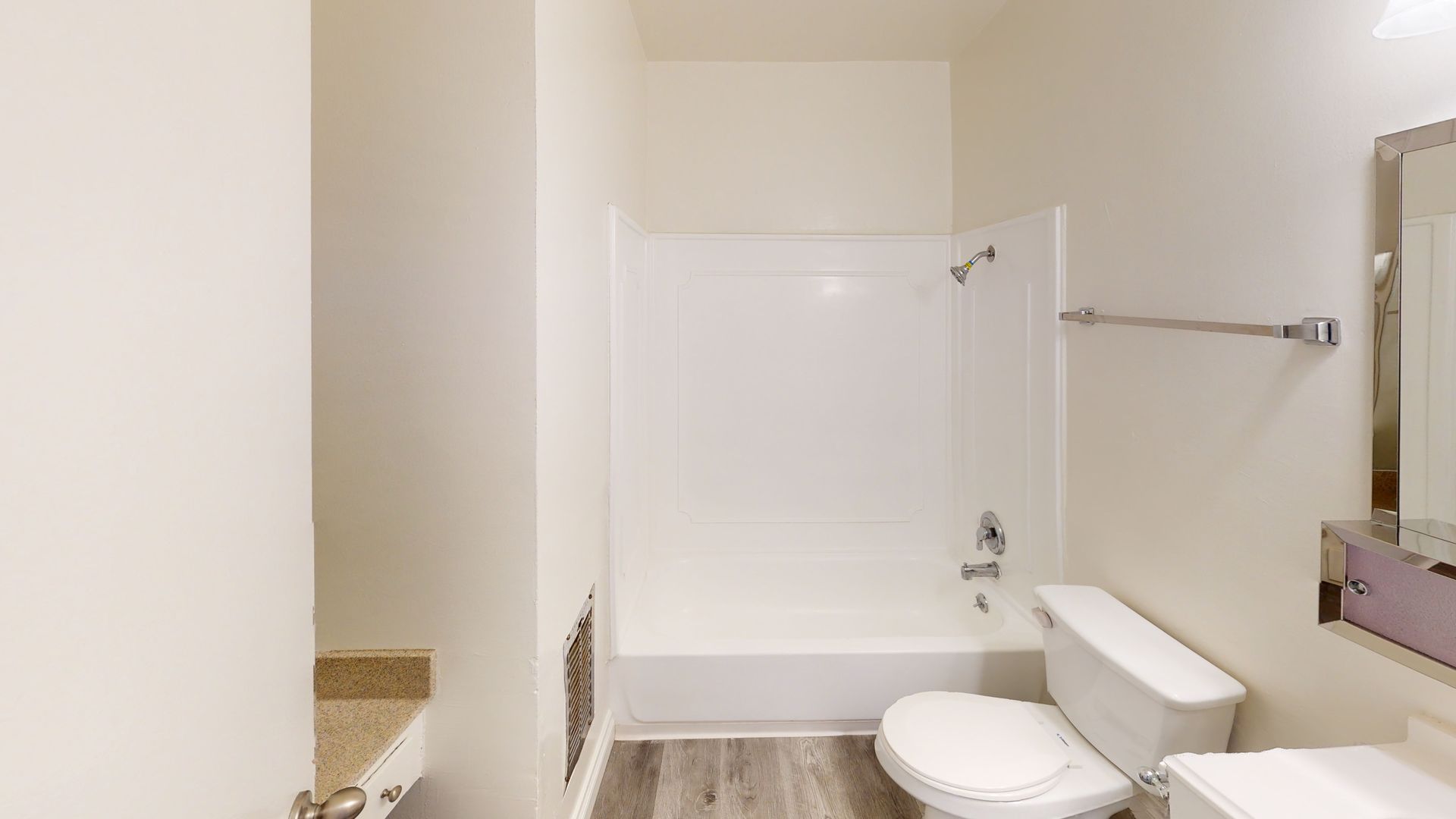 Bathroom with a white tub and toilet, light gray flooring, and a towel bar.