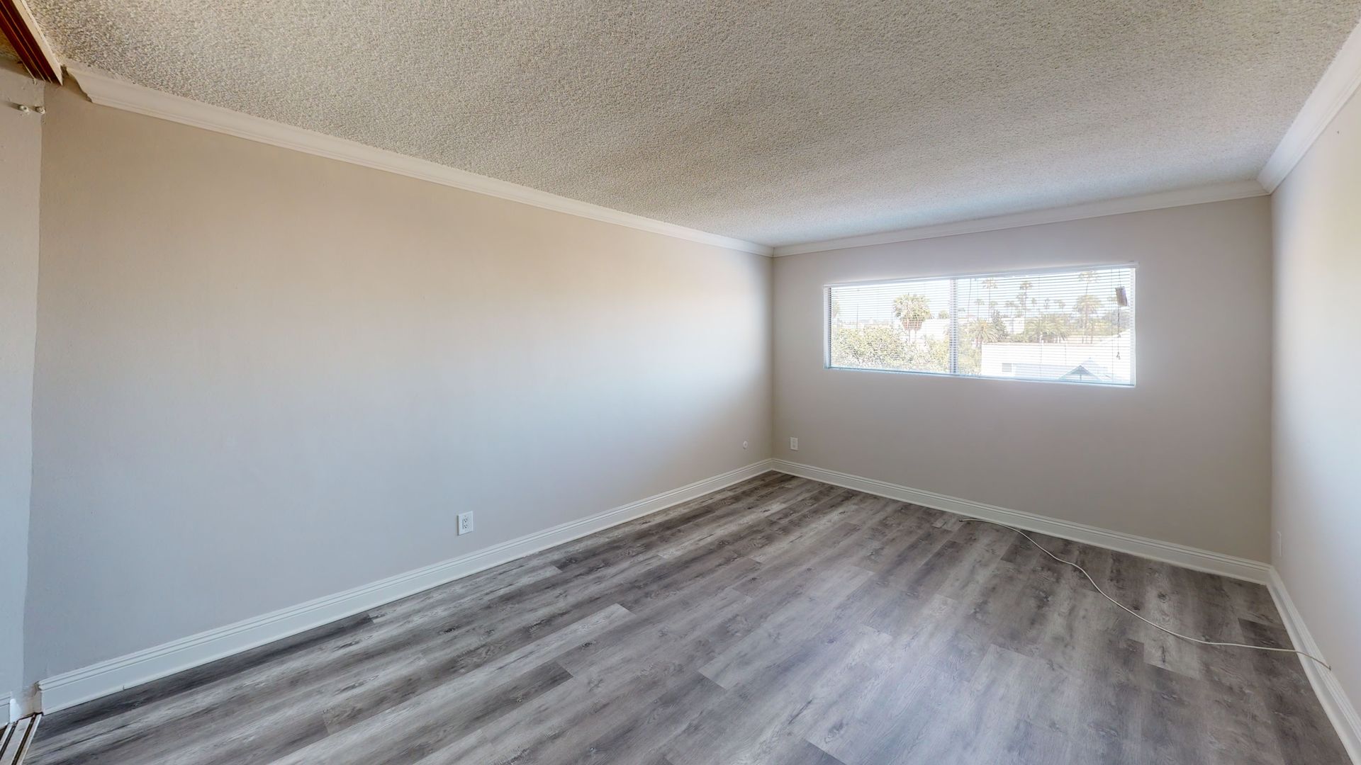 Empty room with gray laminate flooring, white walls, and a window.