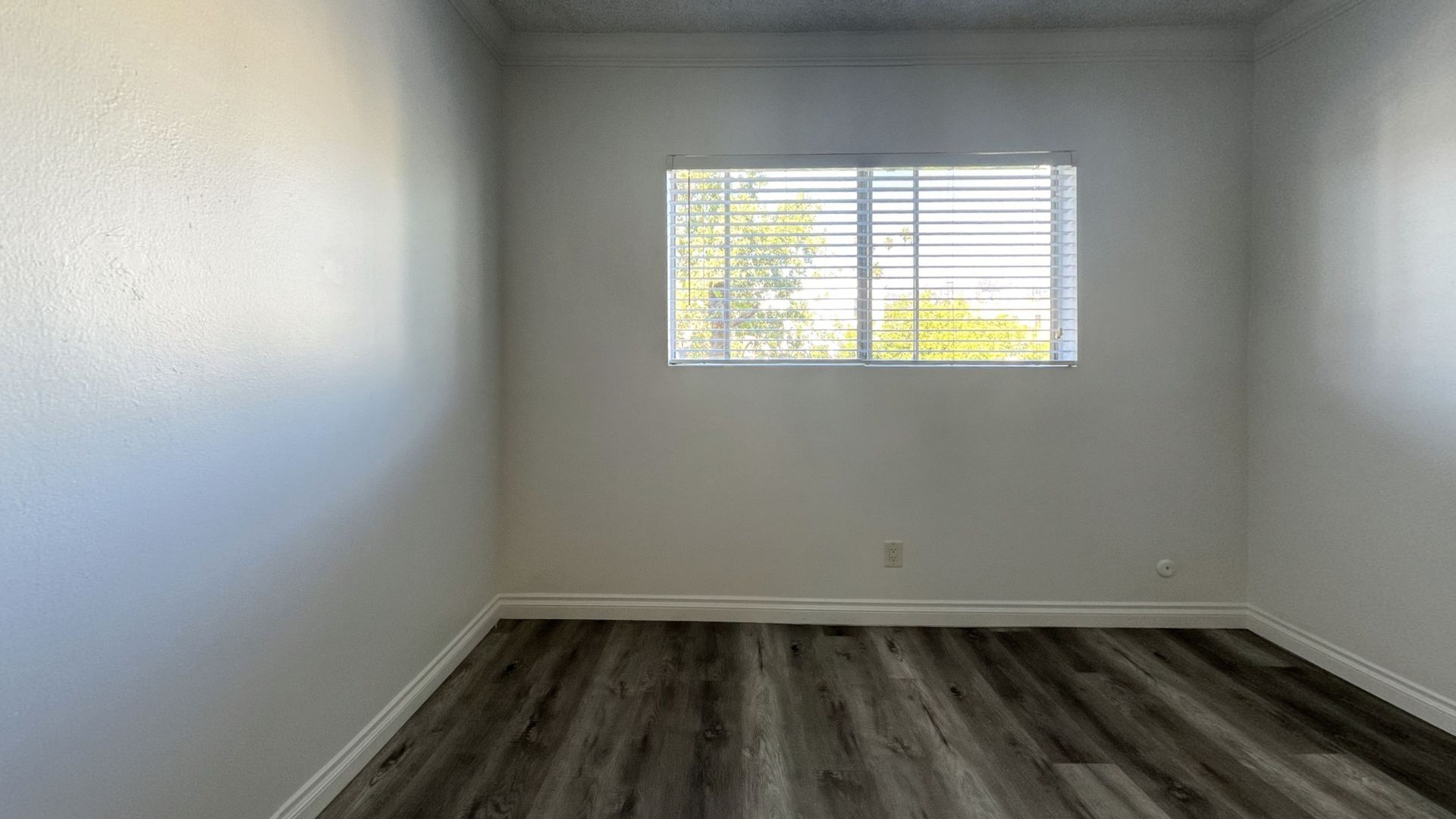 Empty room with white walls, window with blinds, and wood-look flooring.
