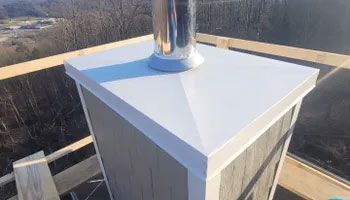Chimney with white cap and stainless steel pipe on a wood-framed roof.