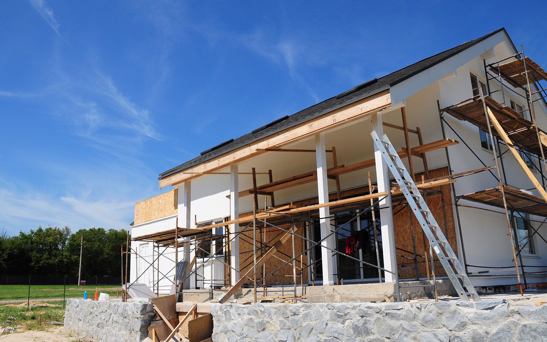 House under construction, white walls, scaffolding, against a blue sky.