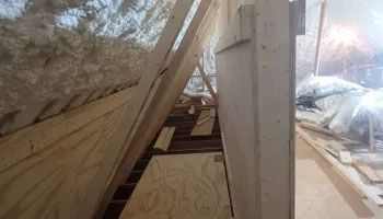 Interior view of attic space under construction with exposed wooden beams and plywood.