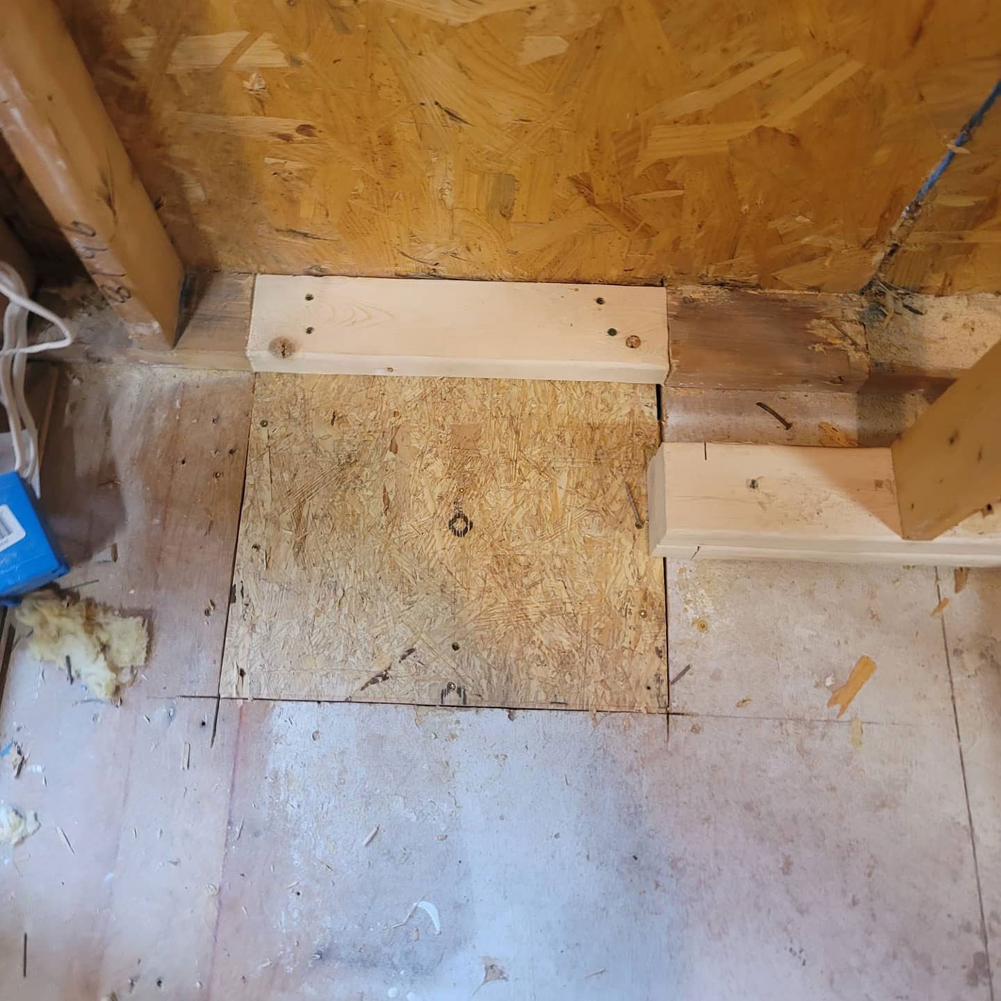 Wooden platform repair in an enclosed space with plywood and wooden beams.