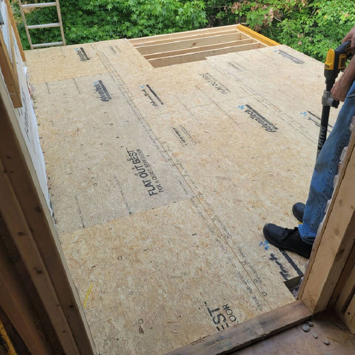 Construction in progress. A person stands inside a wooden structure, installing OSB flooring.