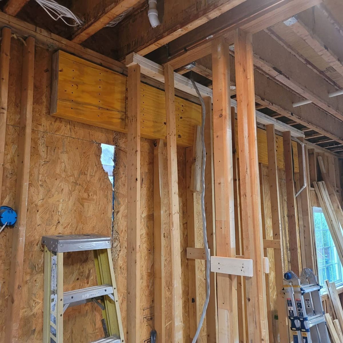 Interior of a building under construction with exposed wooden framing, ladder, electrical work.