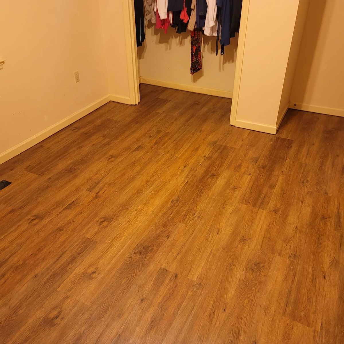 Empty room with wood-look flooring, an open closet with hanging clothes, and beige walls.