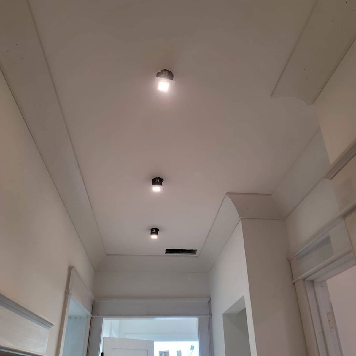 A hallway ceiling with three lights, molding, and a vent. Painted white.