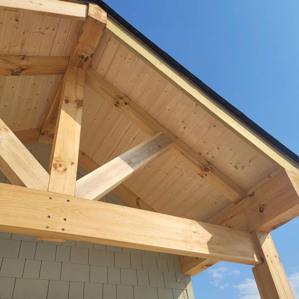 Wooden roof frame with beams and panels, set against a clear blue sky.