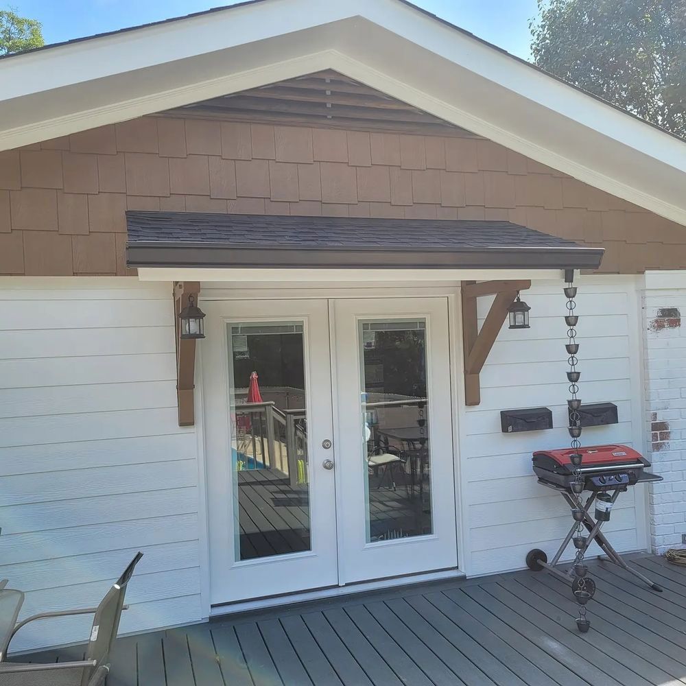 White house with french doors, dark awning, wooden supports. Grill and deck visible.