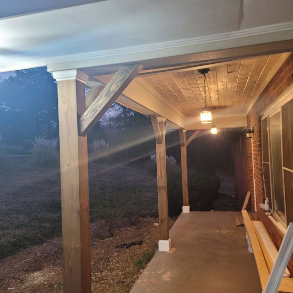 Wooden porch with lights, columns, and exposed beams; brick wall and concrete floor.