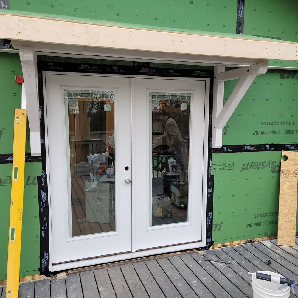White French doors with glass panels installed on a wood deck, under construction, with a wood awning.