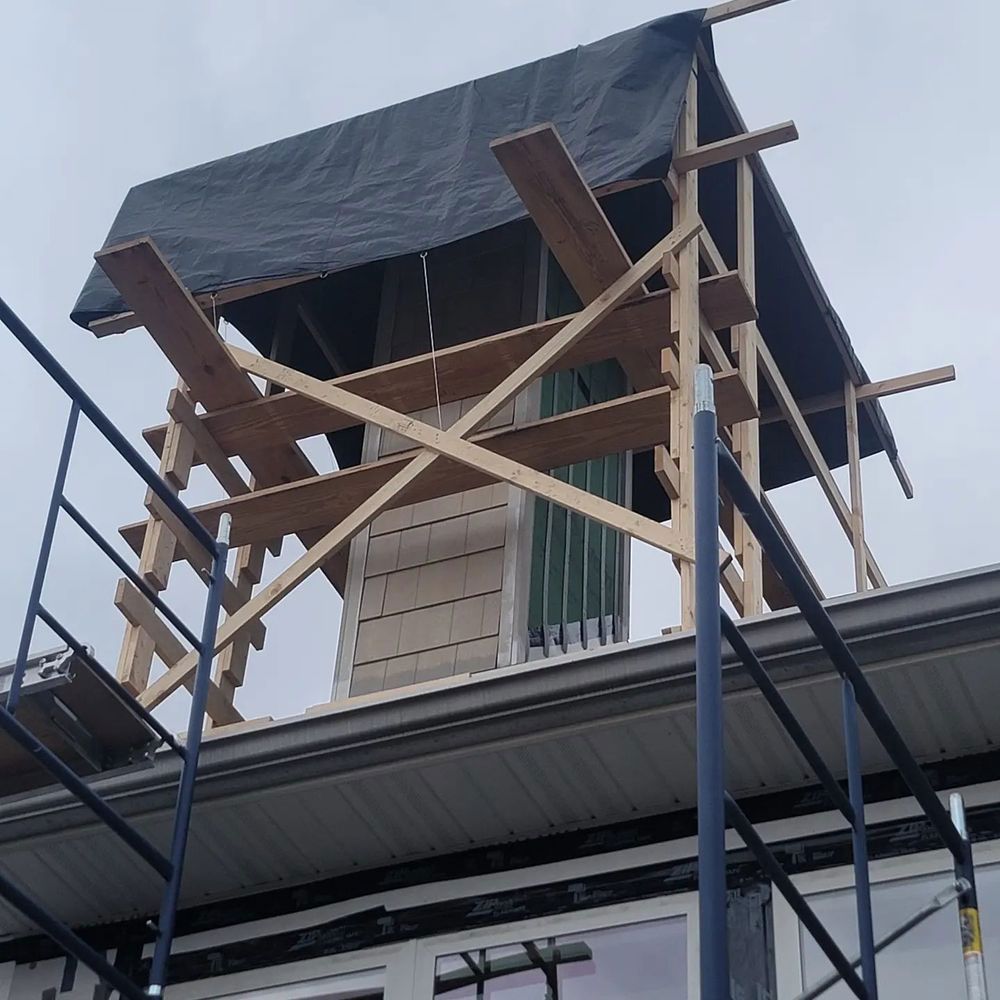 Scaffolding surrounds a chimney covered with a black tarp on the roof of a building.