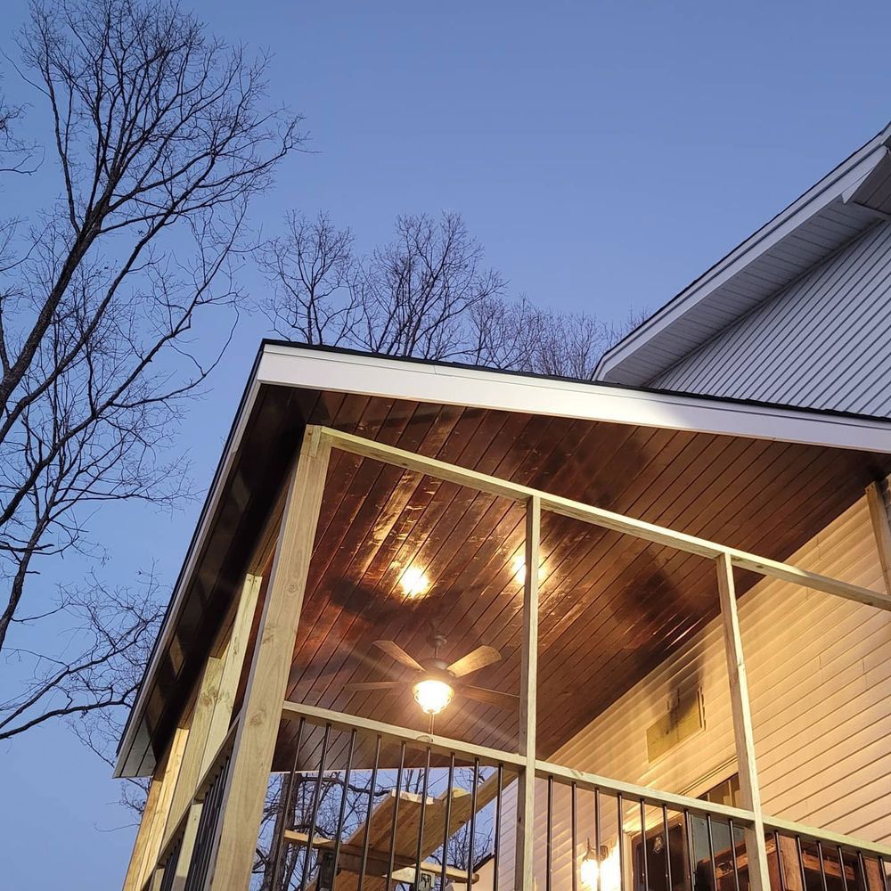 Screened porch with ceiling fan, lights, and railing, attached to a house, against a twilight sky.