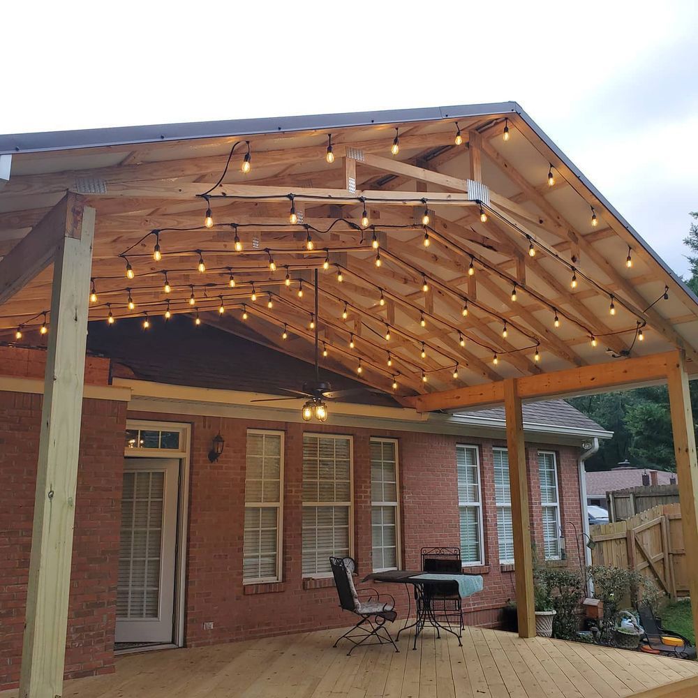 Outdoor patio with string lights on a wooden frame attached to a brick house with a deck and patio furniture.