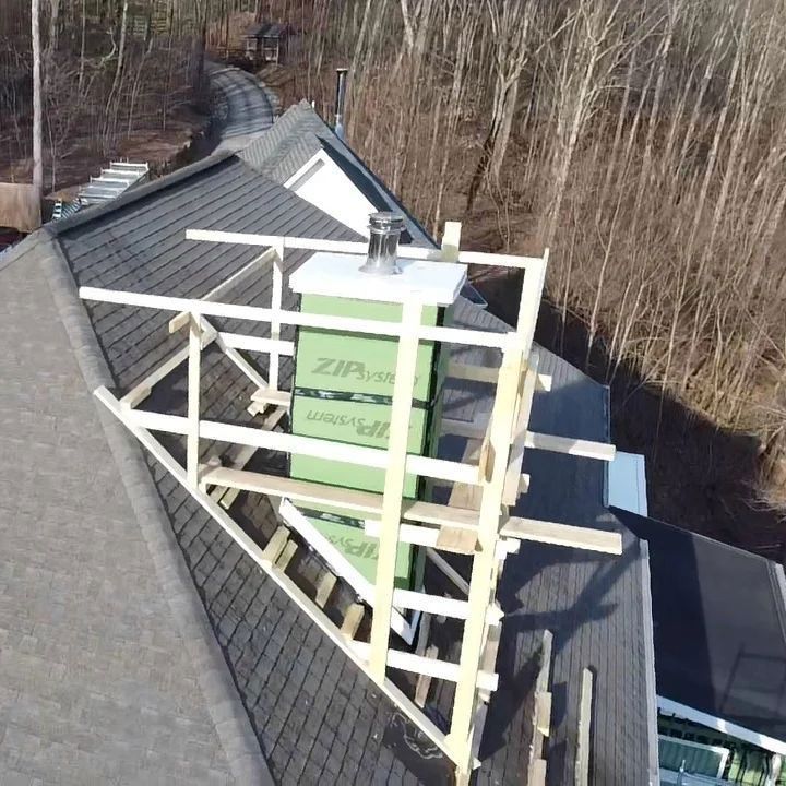 A chimney wrapped in green insulation with temporary wooden scaffolding on a house roof.