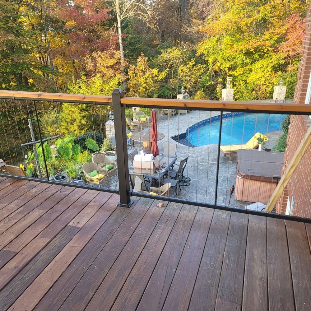 Deck with pool and foliage in the background; cable railings, brown wood, and fall colors.