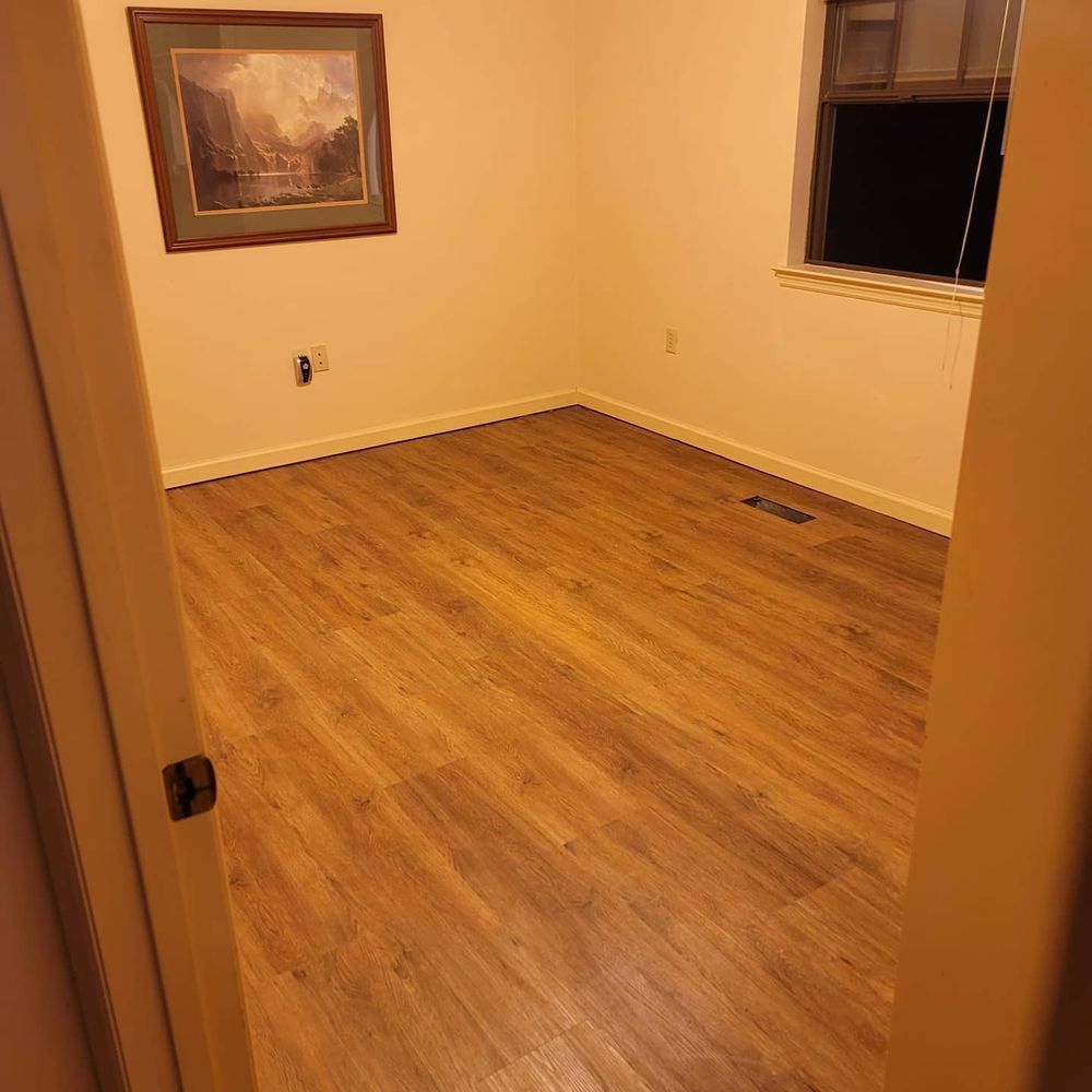 Empty room with wood-look floor, off-white walls, small window, and a framed landscape picture.