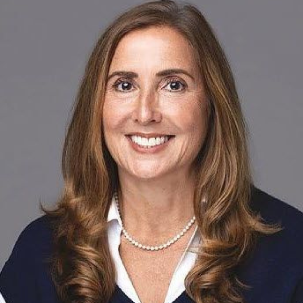A bald man wearing a red jacket is smiling in front of a plant.