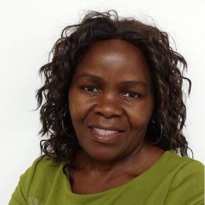 Woman with dark skin, curly hair, smiling, wearing a green top, against a white background.