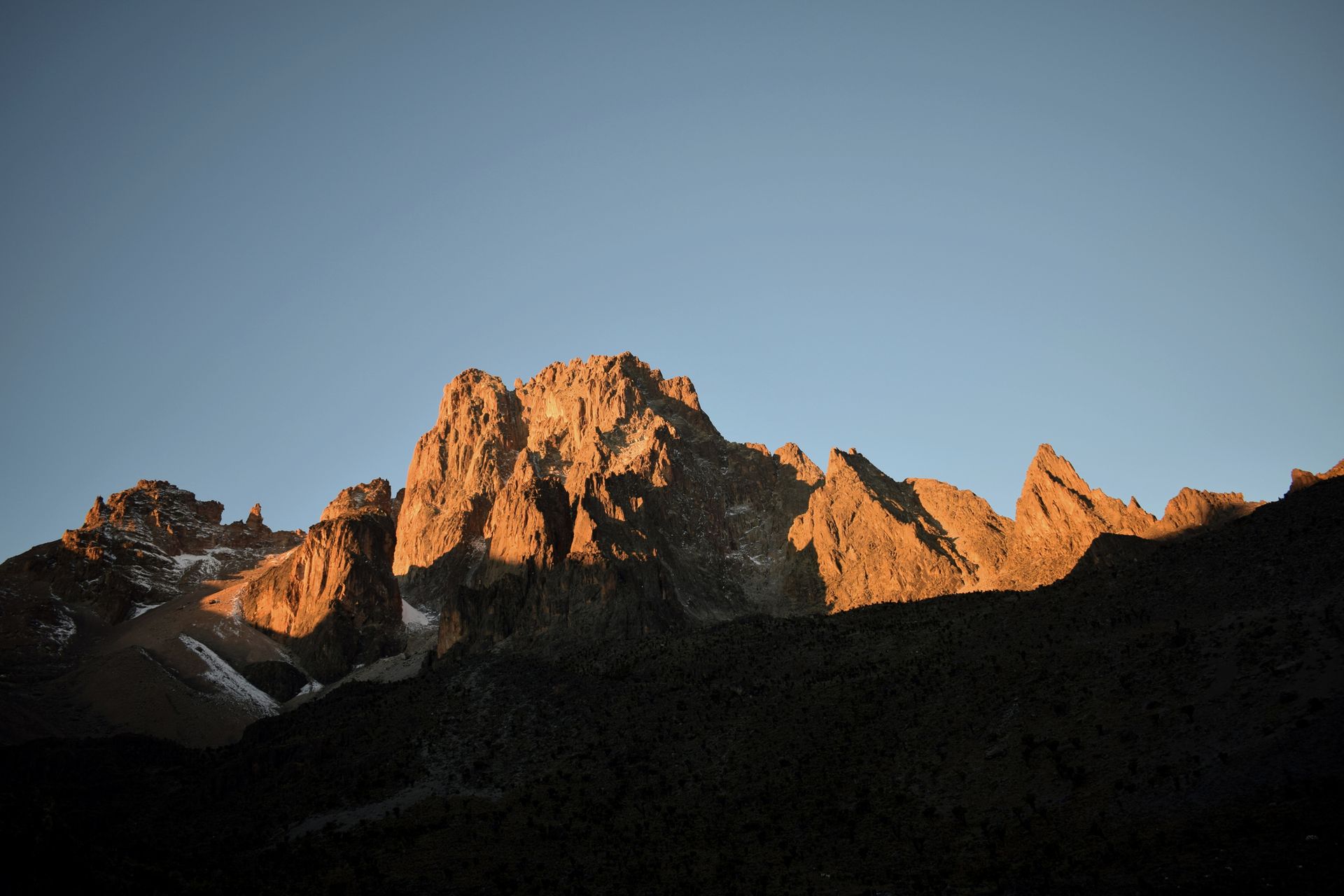 Golden sunlight illuminates rocky mountain peaks against a clear blue sky.