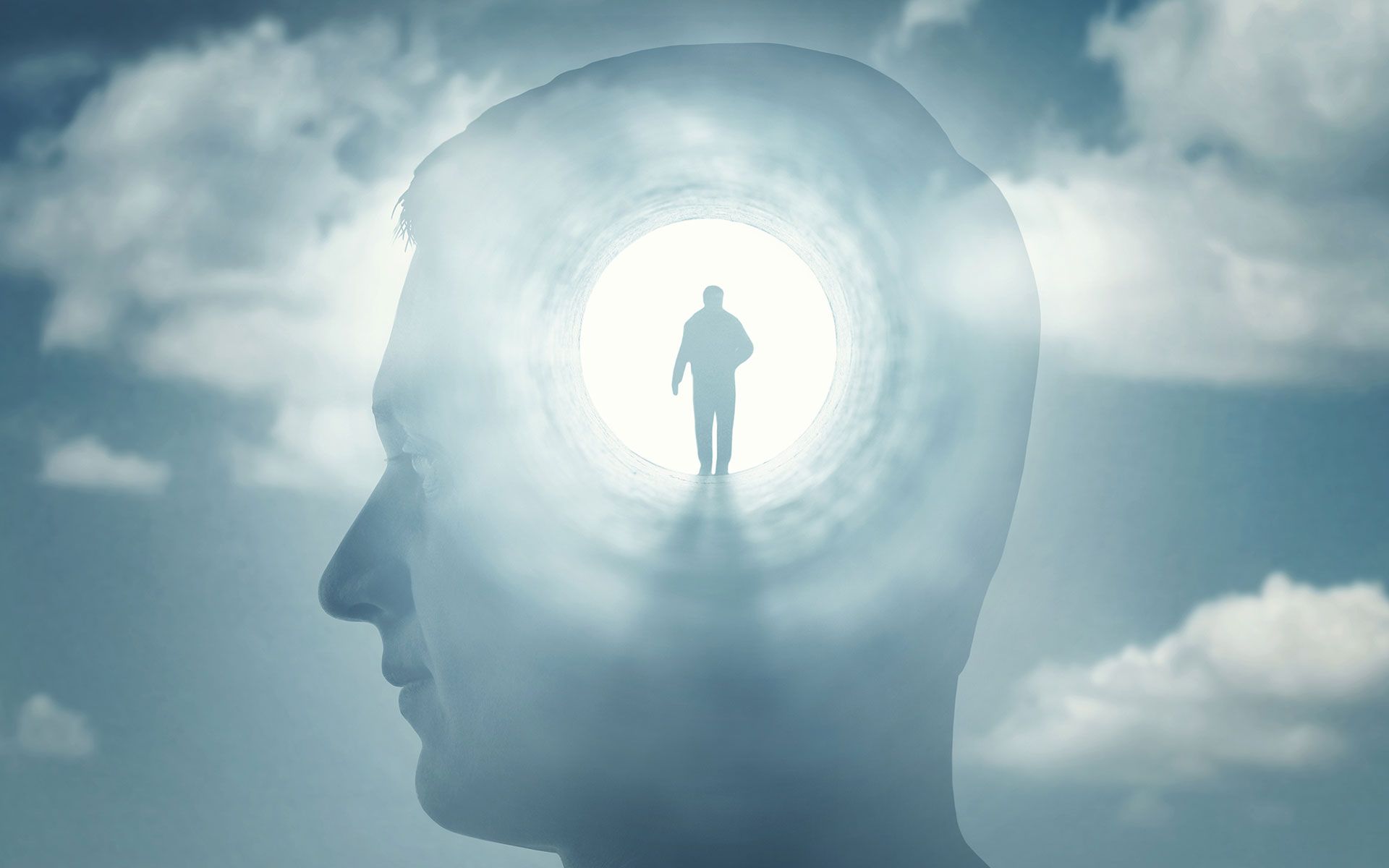 Silhouette of a man walking towards a bright light within a person's head, set against a cloudy sky.