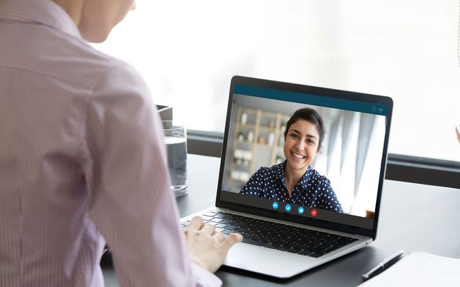 Woman in pink shirt on a video call with a smiling woman in a blue patterned shirt, laptop on a desk.