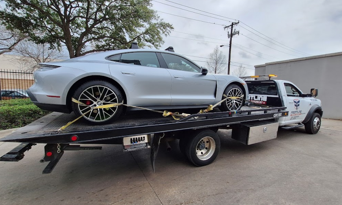 A silver porsche taycan is being towed by a tow truck.