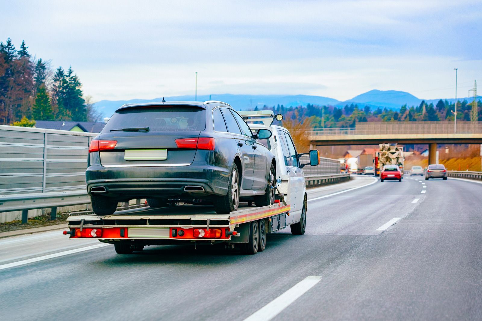 A black car being towed on a flatbed tow truck on a highway.