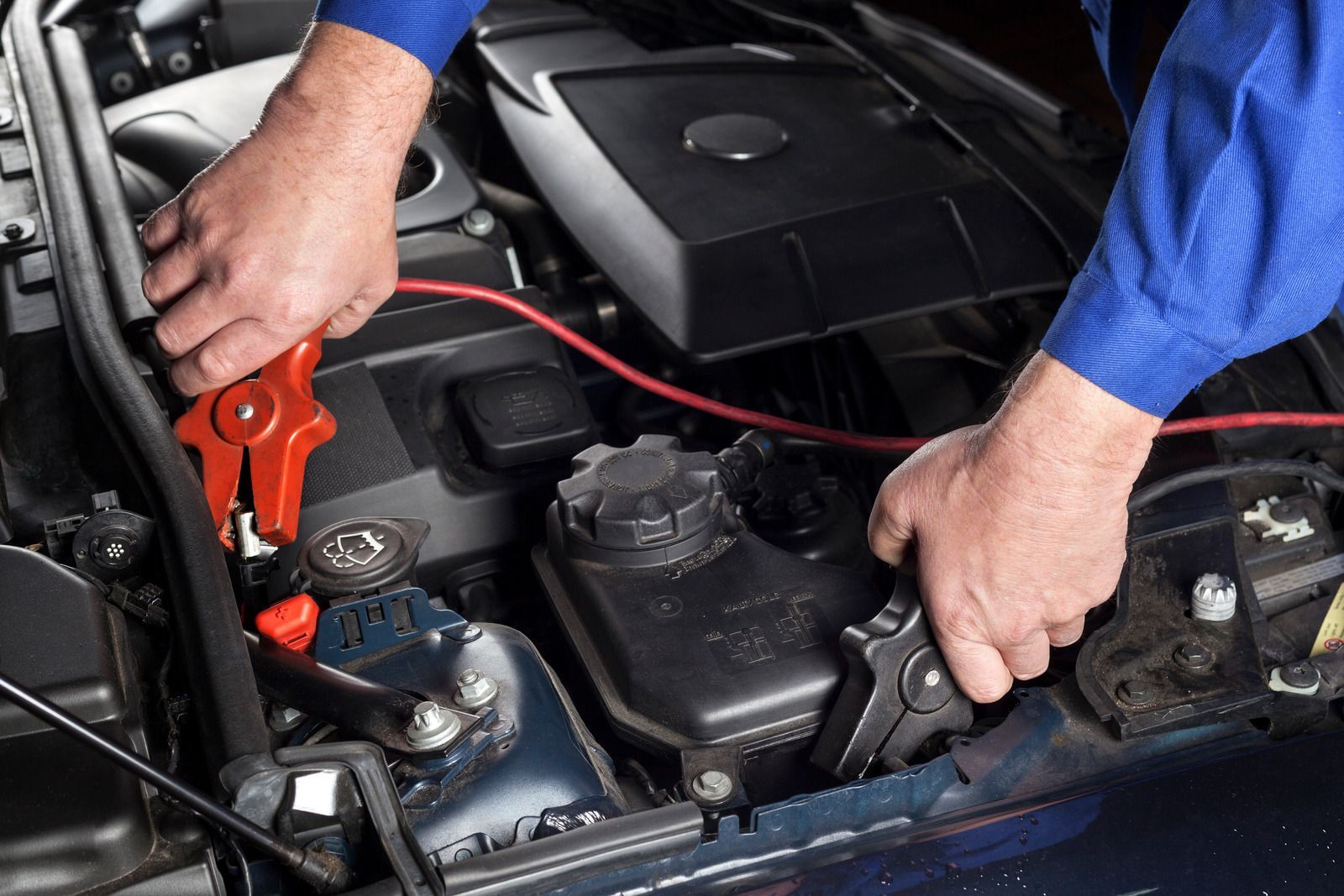 Hands connecting jumper cables to a car battery in a vehicle's engine bay; red and black cables.