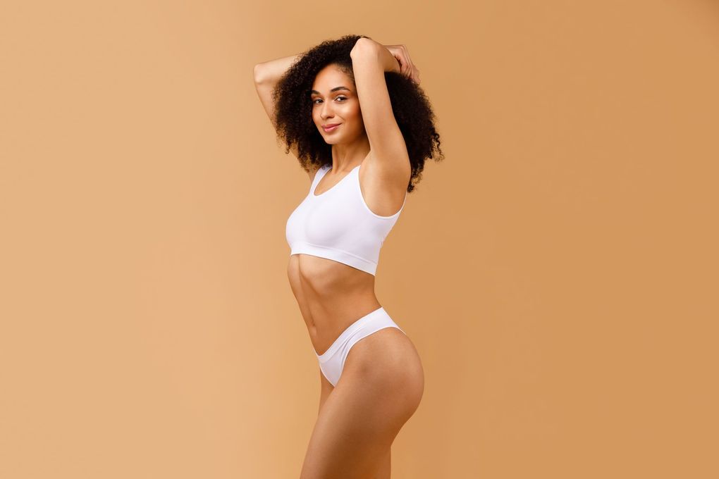 a woman in white underwear is standing on a beige background .