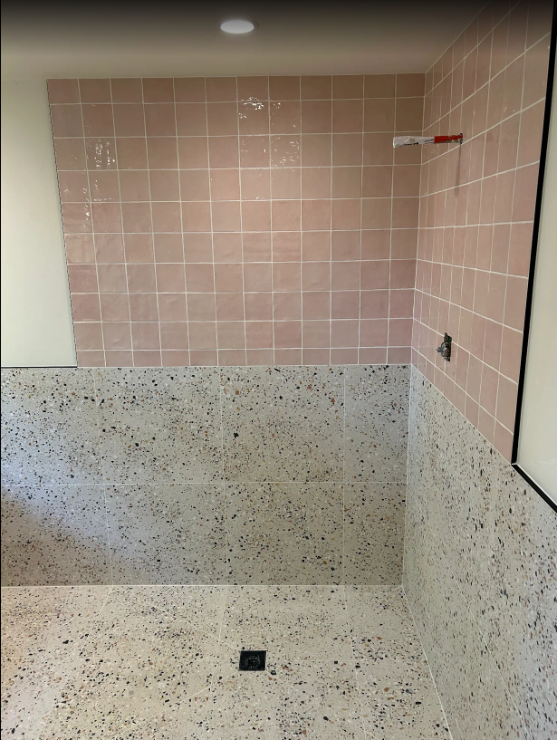 Pink and gray tiled shower alcove with a recessed shelf and floor drain