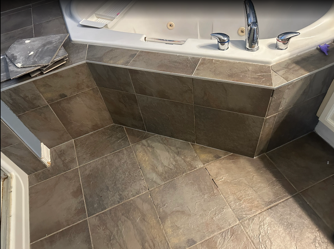 Stone-tiled bathroom with a built-in shower bench and metal fixtures by the tub.
