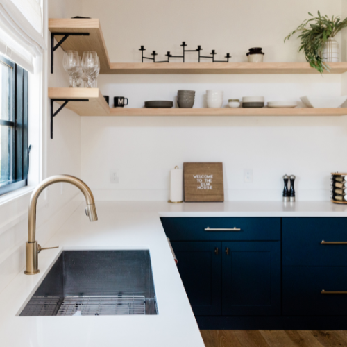 Modern kitchen with white countertops, navy cabinets, brass faucet, and open shelves