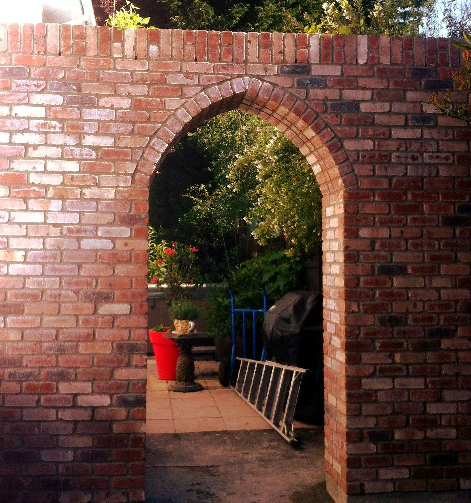 A brick wall with an archway leading to a garden