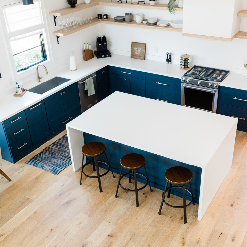 Top-down view of kitchen with navy cabinets, white island, and three stools on light wood floors.