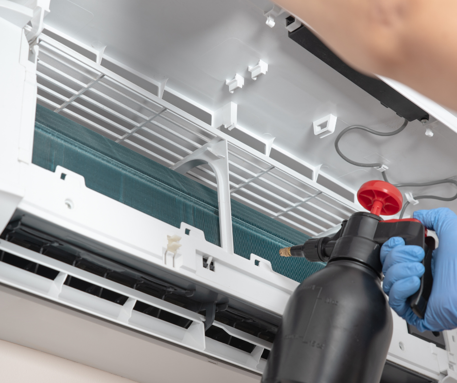 A person is cleaning an air conditioner with a spray bottle.