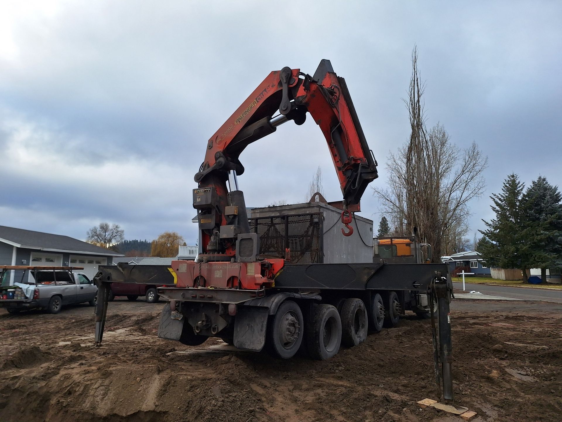 A red crane truck on a muddy job site lifting a large rectangular concrete block.