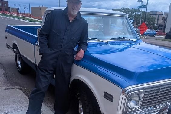 Person leaning on a blue and white vintage pickup truck outdoors. | Exodus Motor Works LLC