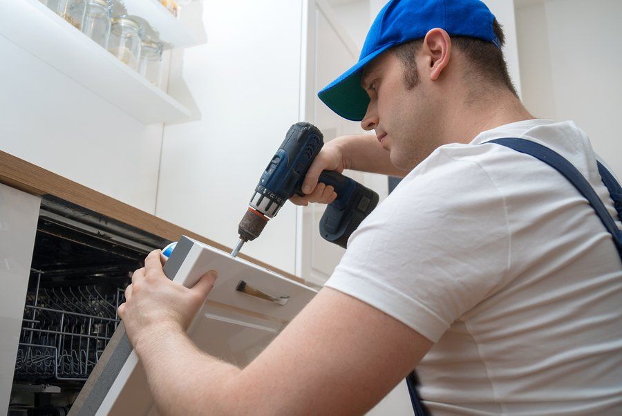 repairman fixing the dishwasher with a cordless drill