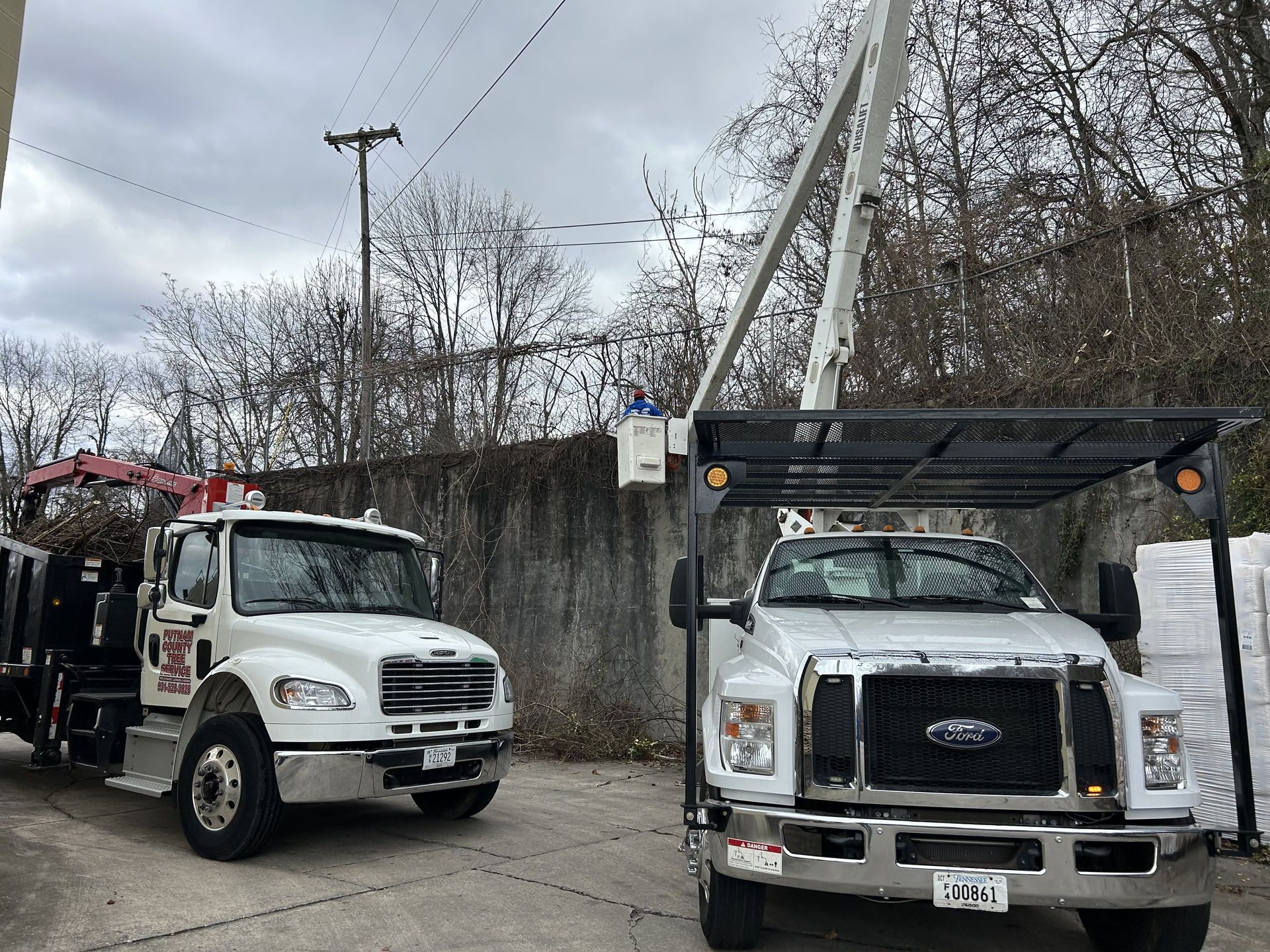 Two white work trucks parked outdoors, one with an elevated platform.