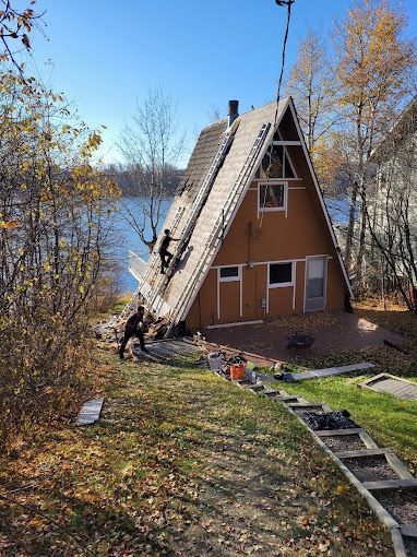 A man is standing on the roof of an a frame house.