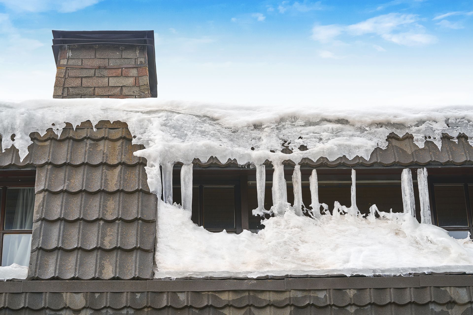 The roof of a house is covered in snow and icicles.