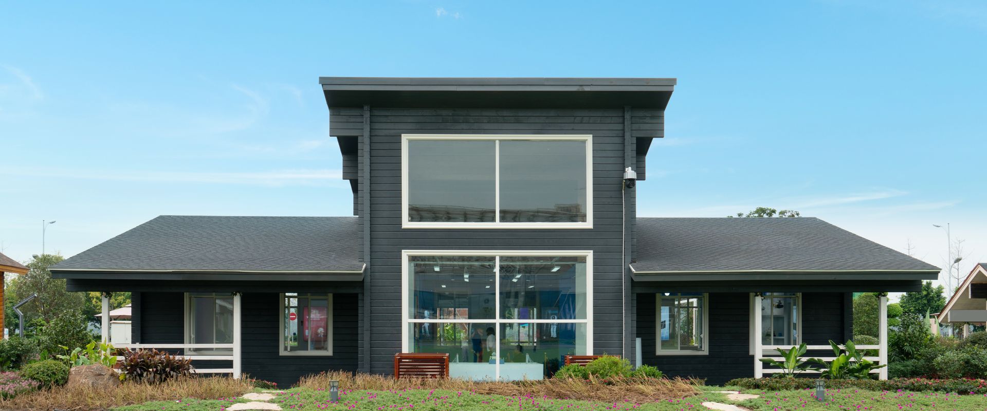 A black house with a lot of windows is sitting on top of a lush green field.