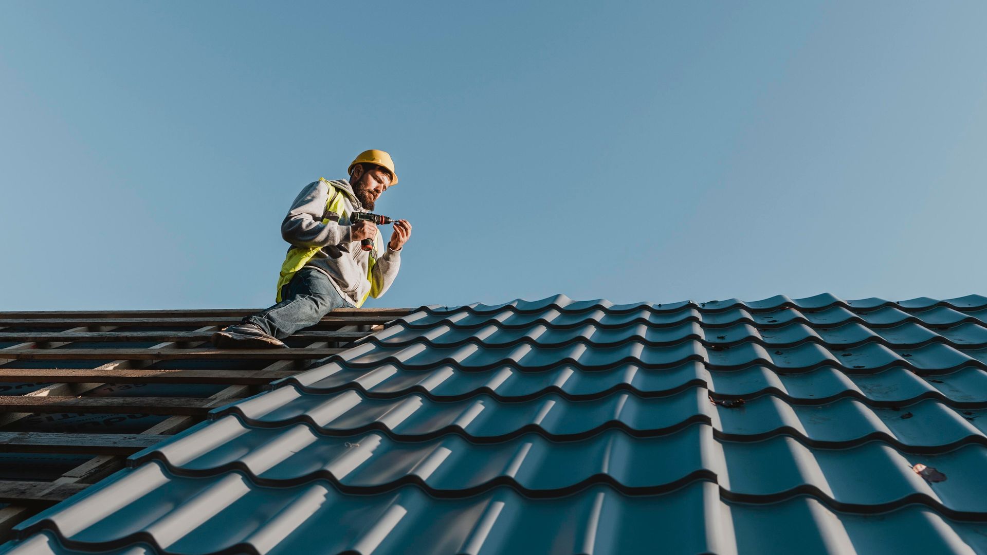 A man is standing on top of a roof holding a hammer.