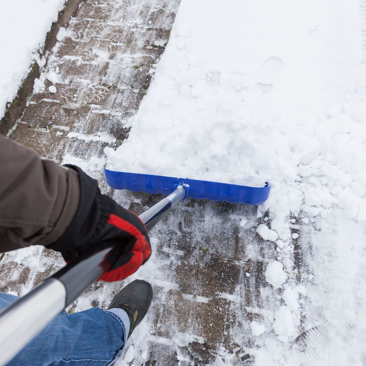 A person wearing gloves is shoveling snow on a sidewalk