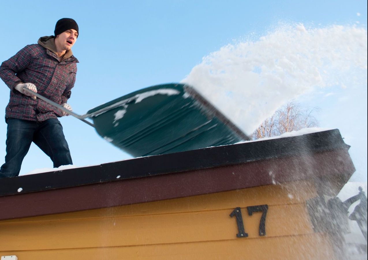 A man is shoveling snow from the roof of a building with the number 17 on it