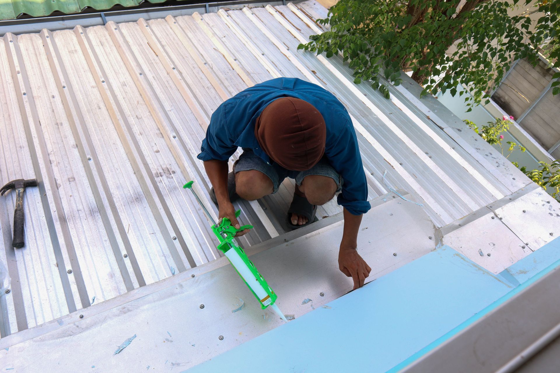 A man is working on a roof with a green sealant