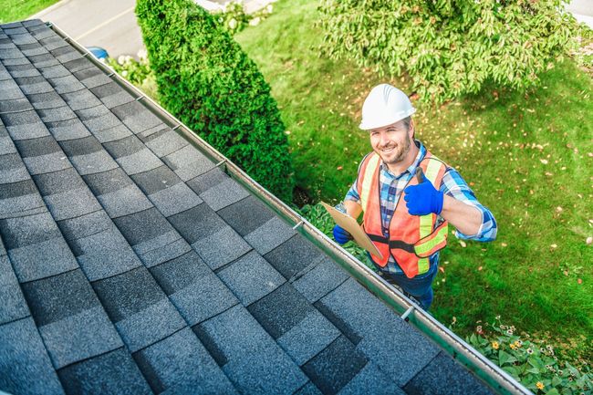 A man is standing on top of a roof holding a clipboard.