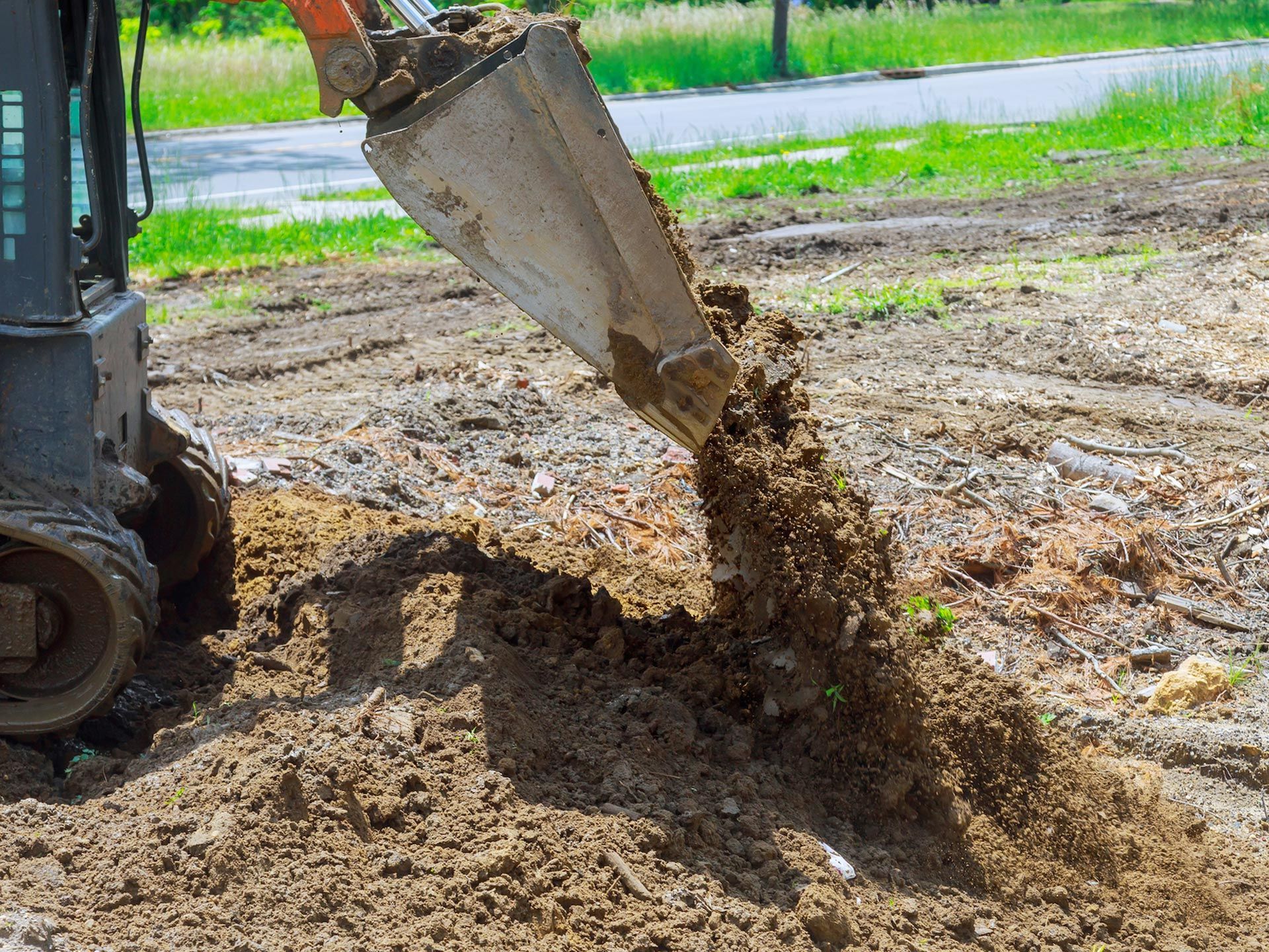 A small construction vehicle dumping soil onto a dirt ground, near a grassy area.