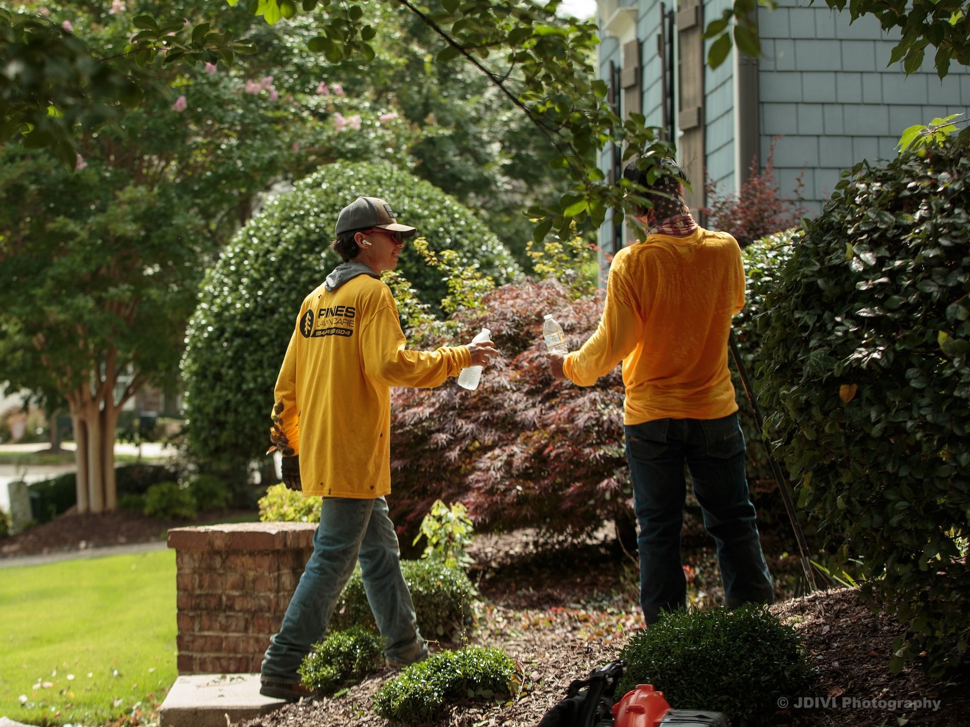 Two people in yellow shirts holding water bottles outdoors; landscaping work.